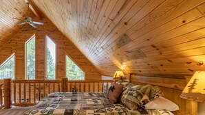 Un dormitorio de cabaña de madera con una cama, una mesita de noche, una lámpara y un ventilador de techo.