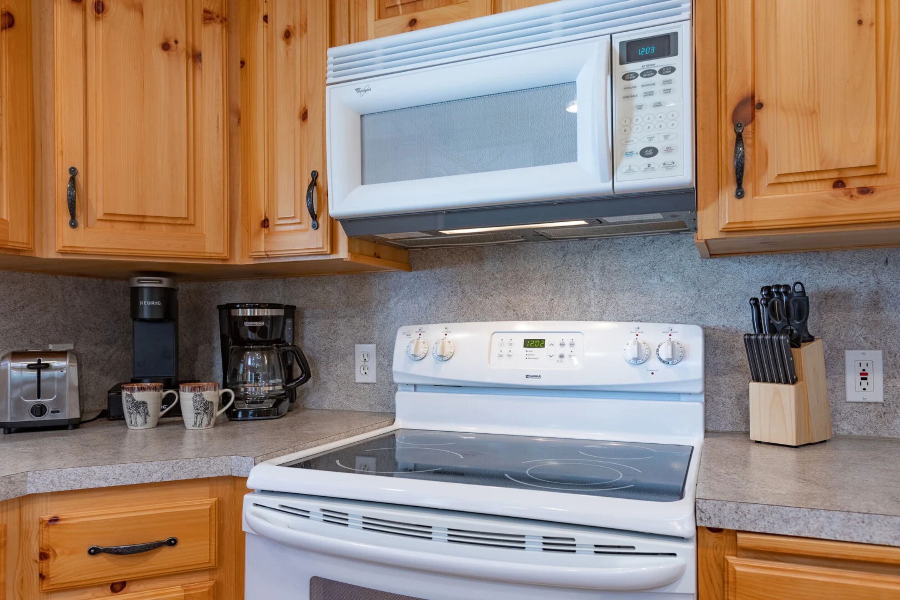 A kitchen with wooden cabinets, a microwave, a coffee maker, a toaster, and a knife block.