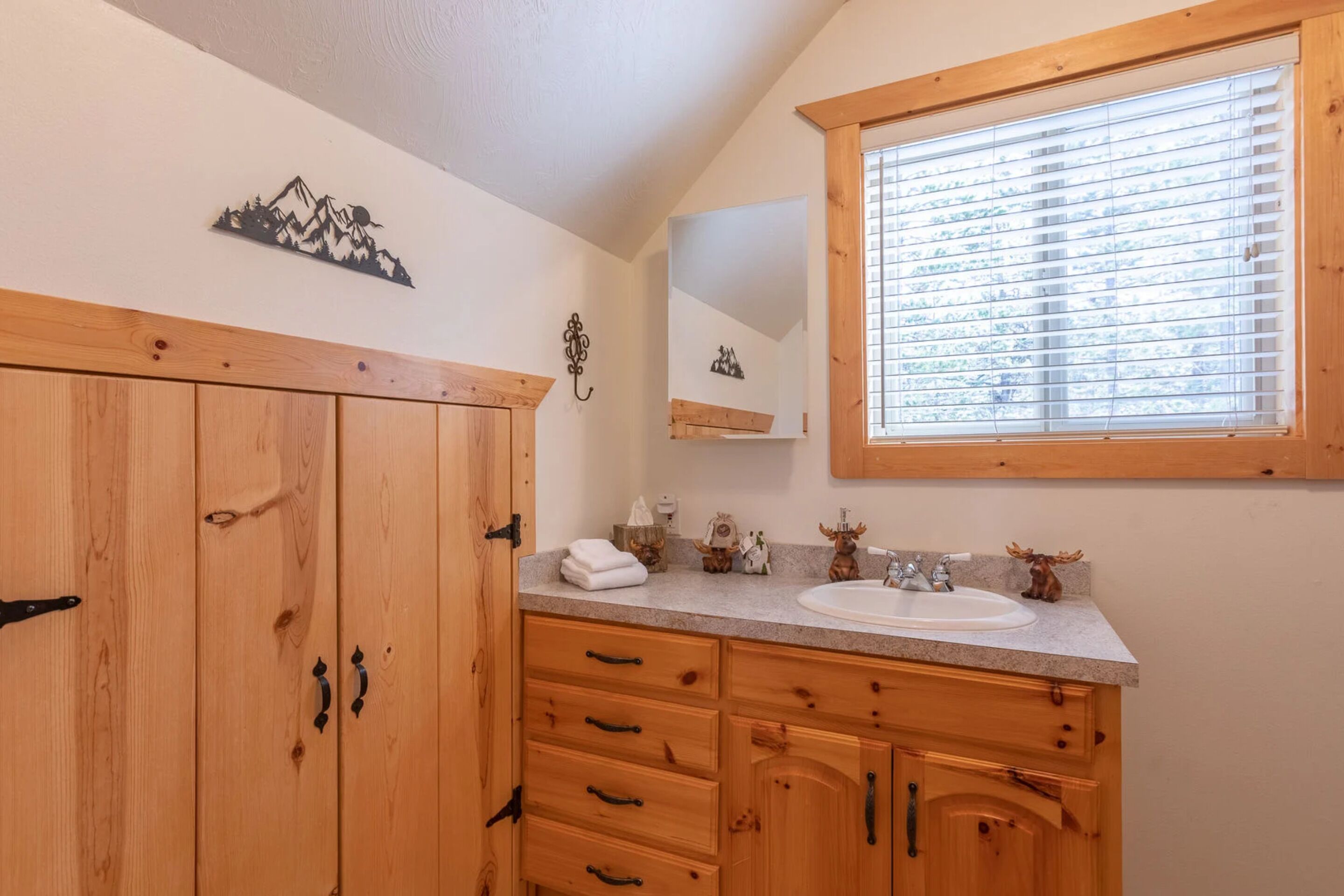 Une salle de bain avec des meubles en bois, un lavabo et une fenêtre avec des stores.