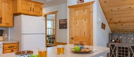 A kitchen with wooden cabinets, a refrigerator, a dining table with plates and glasses, and a wine rack.
