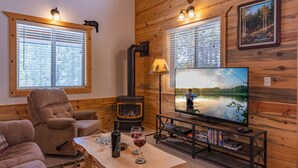 Un interior de cabaña acogedor con chimenea, televisor y una zona de estar cómoda.