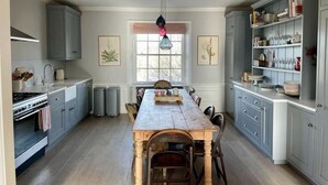 A spacious kitchen with a central island, grey cabinetry, and a dining area with a long table and chairs.