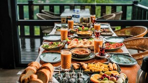 A dining table set with various dishes, drinks, and bread, overlooking a scenic landscape. - GAFULLUK TATİL KÖYÜ (Arakli)