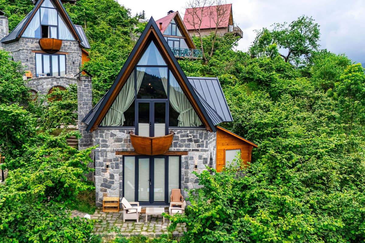 A stone house with a steep roof, large windows, and a balcony.