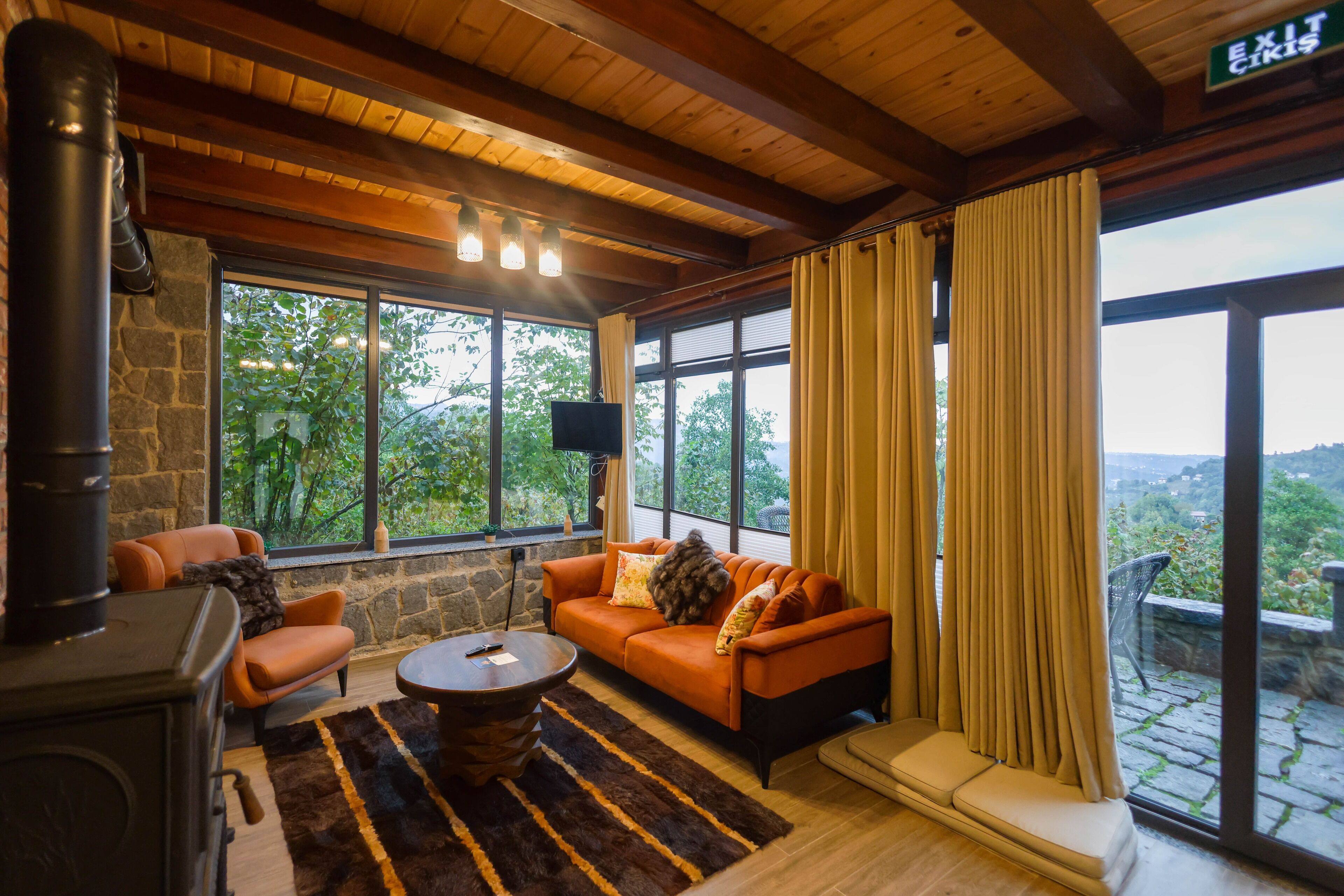 A cozy room with a stone wall, a fireplace, a sofa, and a large window with curtains.