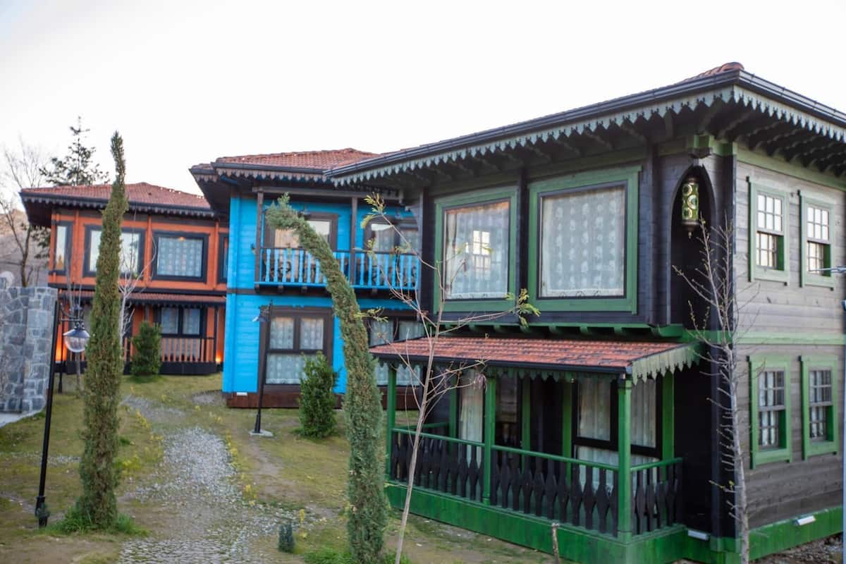 A row of traditional wooden houses with balconies, a stone wall, and a gravel path.