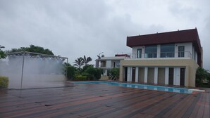 A rooftop pool area with a wooden deck, a water feature, and a modern building with balconies. - Chandan Van Club and Resort - Navsari (Navsari)