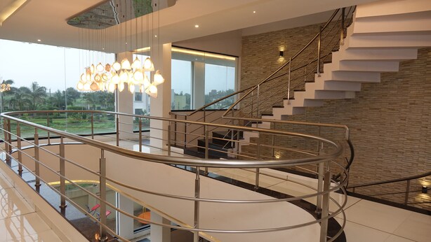 A modern interior with a glass balustrade, a staircase with metal railings, and a view of greenery outside. - Chandan Van Club and Resort - Navsari (Navsari)