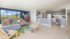 Ein modernes Wohnzimmer mit Sofa, Sessel und einem kleinen Couchtisch. Es gibt eine Küchenzeile mit Kühlschrank, Herd und Spüle.
