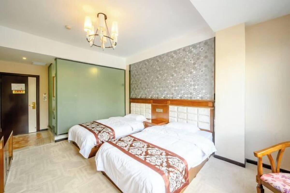 Quarto de hotel com duas camas, cabeceira de madeira, porta verde e parede estampada.