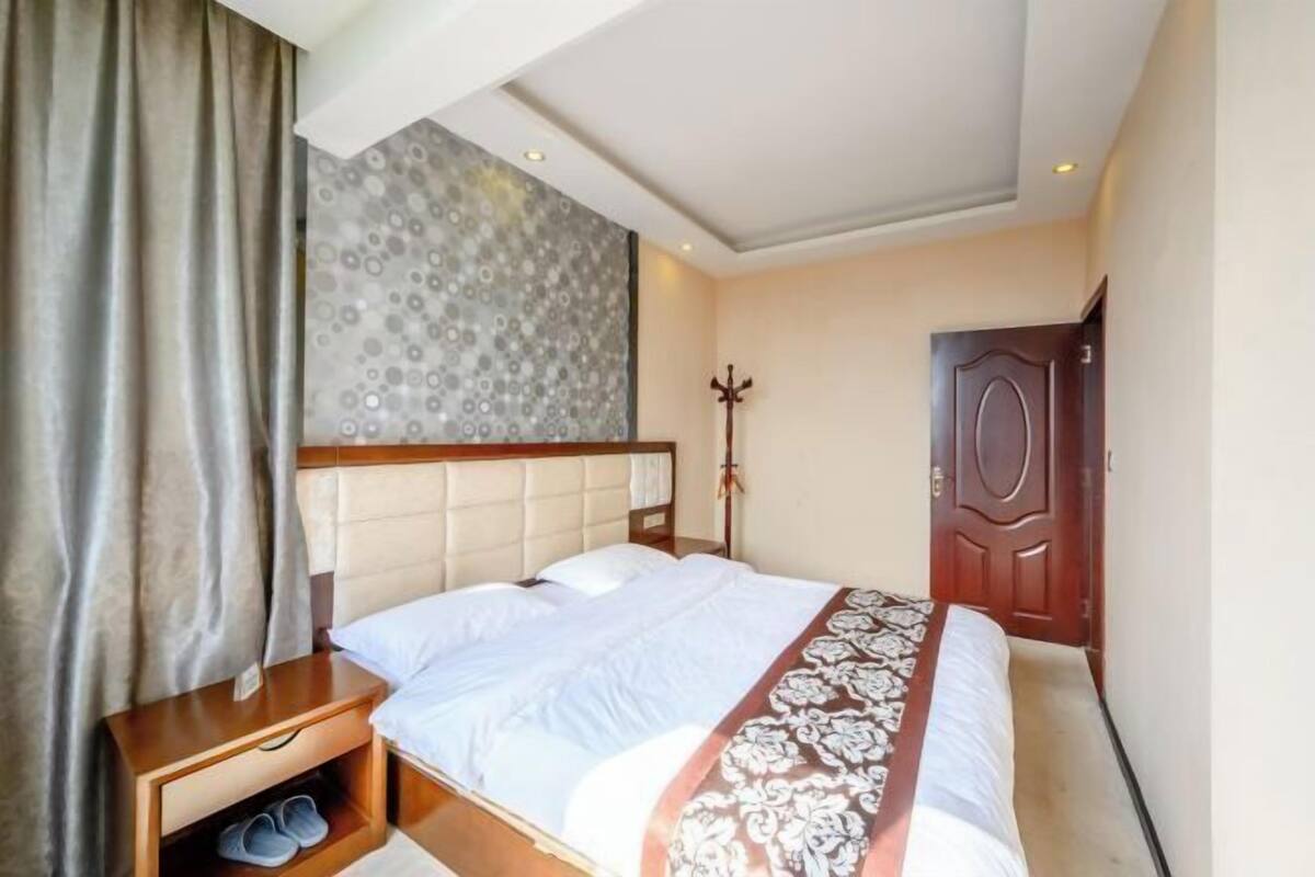 Quarto de hotel com uma cama, uma mesa de cabeceira de madeira, um porta-roupas e uma porta.