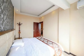 A hotel room with a bed, a coat rack, and a door.