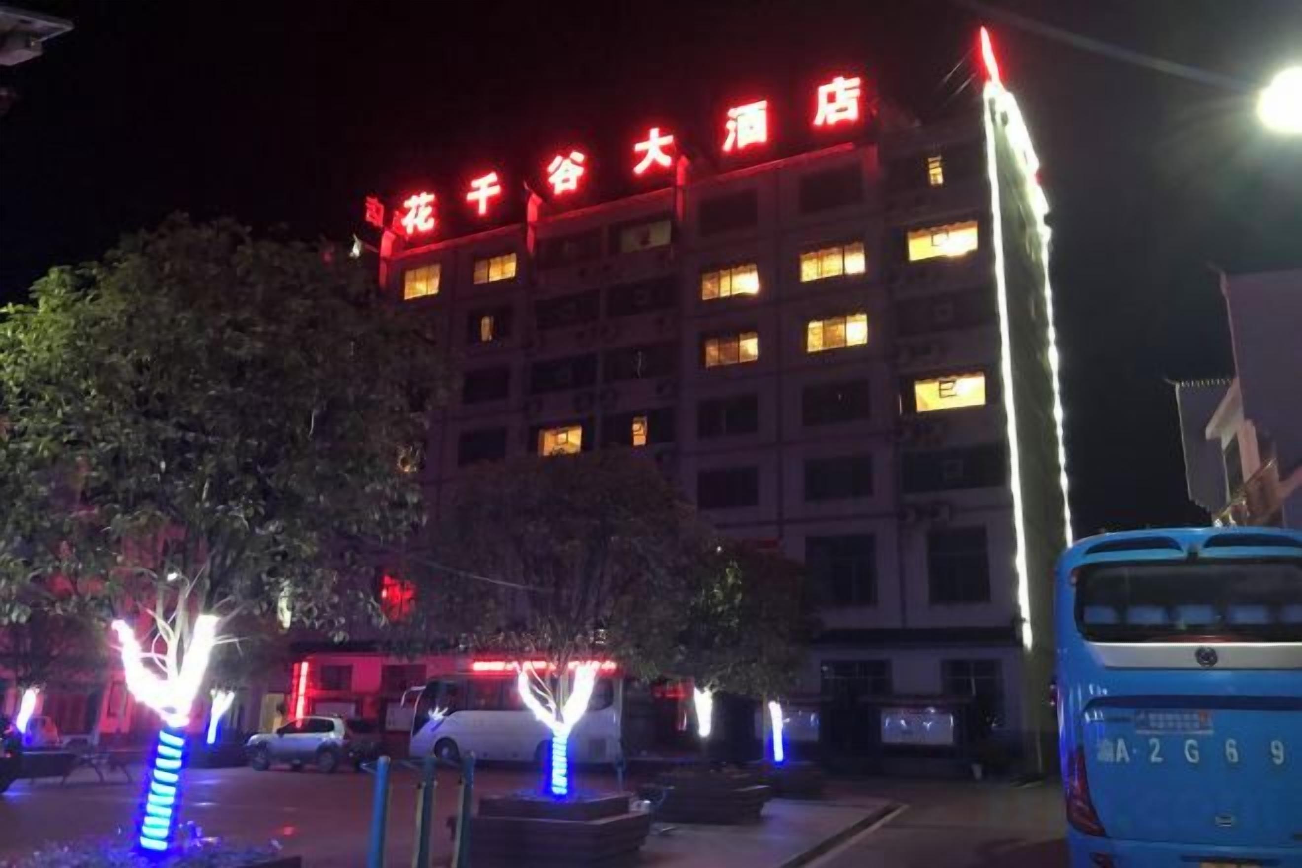 A hotel with illuminated signage, a parking lot, and a blue bus.