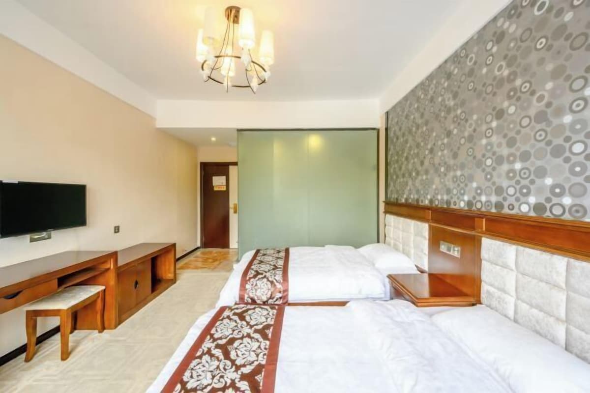 A hotel room with a bed, a TV, a desk, and a patterned headboard.