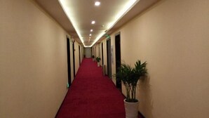 A hotel hallway with a red carpet, beige walls, and recessed lighting.