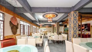 A spacious restaurant with multiple tables and chairs, a patterned ceiling, and a decorative wall.