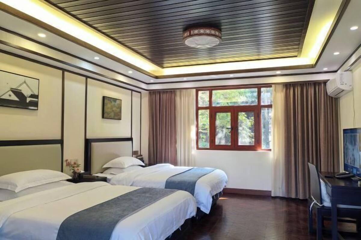 Une chambre d’hôtel avec deux lits, un bureau, une télévision, une fenêtre avec des rideaux et un plafond doté d’un éclairage encastré.