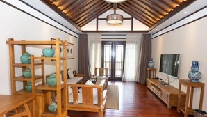 A room with a wooden floor, a sofa, a TV, and a shelf with decorative items. - Zunyi Fengxiangyuan Hotel (Zunyi)