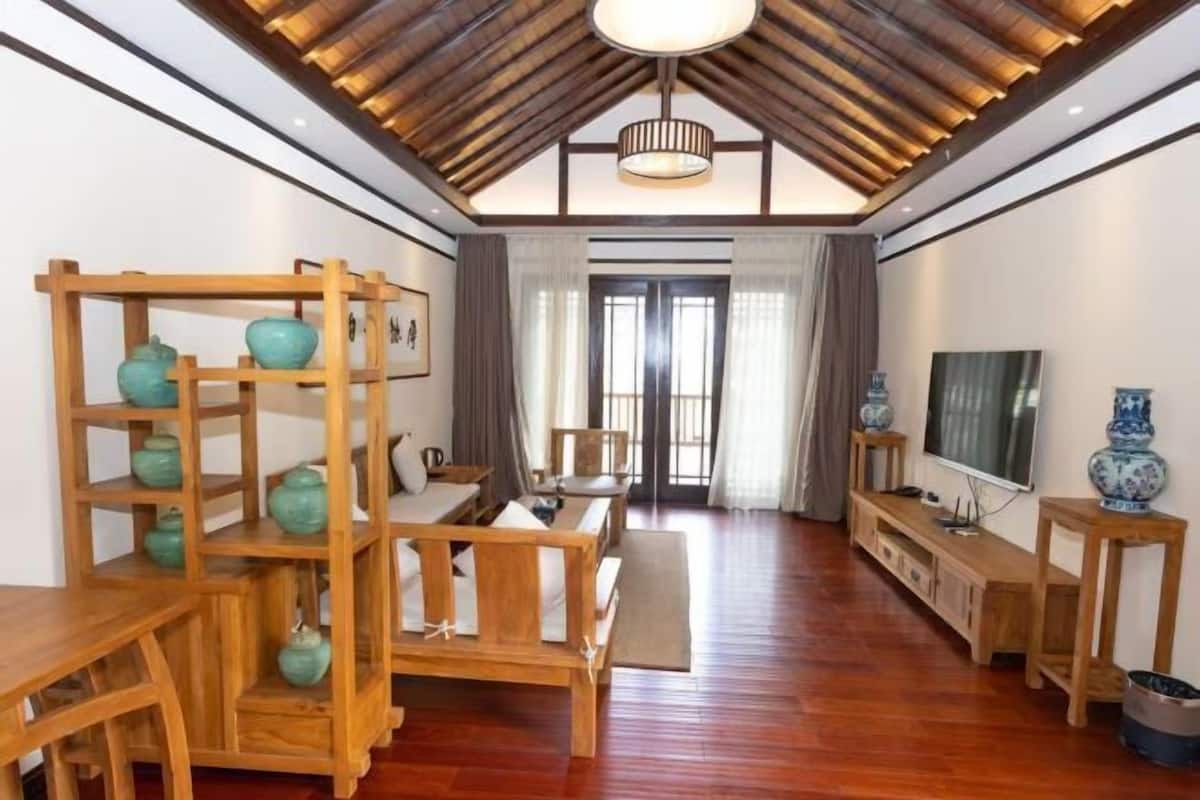 Une pièce avec un plancher en bois, un canapé, un téléviseur et une étagère ornée d’objets décoratifs.