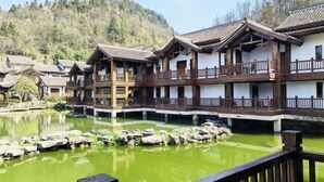 A traditional building with multiple balconies, a pond with rocks, and a forested hillside in the background. - Zunyi Fengxiangyuan Hotel (Zunyi)