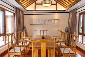 A conference room with a wooden table and chairs, a ceiling light, and a framed calligraphy piece on the wall.