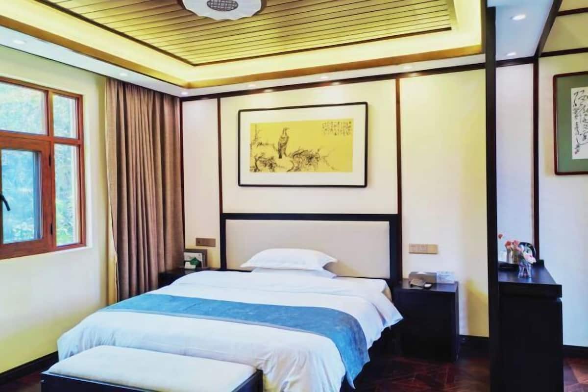 Une chambre d’hôtel avec un lit, une table de chevet, une fenêtre, un rideau et une œuvre d’art encadrée accrochée au mur.