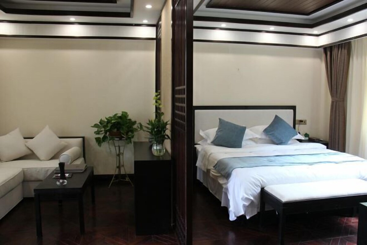 A hotel room with a bed, a sofa, a small table, and a potted plant.