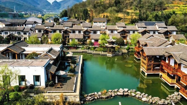 A traditional village with wooden houses, a central pond, and mountains in the background. - Zunyi Fengxiangyuan Hotel (Zunyi)