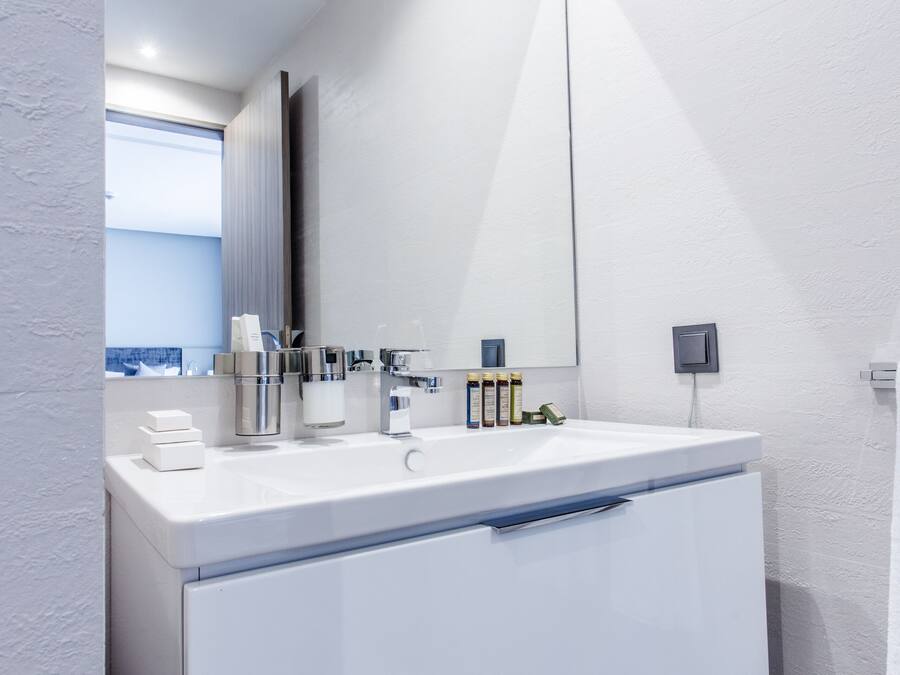A modern bathroom with a white vanity, a large mirror, and a window providing a view.