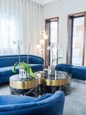 A modern living room with blue sofas, a marble coffee table, and white orchids. - Makass Appart Hotel (Rabat)