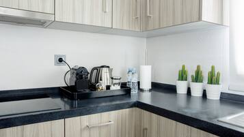 A modern kitchen with light wood cabinets, a black countertop, and a coffee maker. There are three potted cacti on the counter.