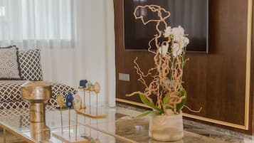 Un salon moderne avec une table basse en verre, un téléviseur à écran plat fixé à un mur en bois et une composition florale décorative avec des orchidées.