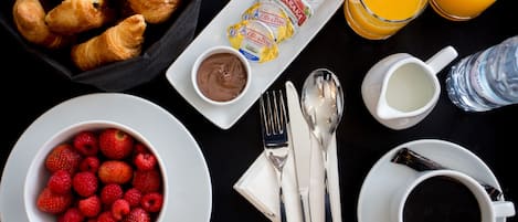 Desayuno con cruasanes, fresas, frambuesas, crema de chocolate, zumo de naranja, leche, café y una botella de agua.