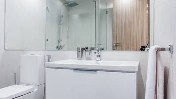 Un baño moderno con cabina de ducha de vidrio, un lavamanos blanco y un inodoro.