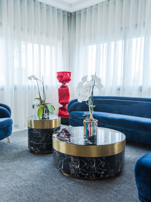 Una sala moderna con un sofá azul, dos mesas de centro de mármol y orquídeas blancas.