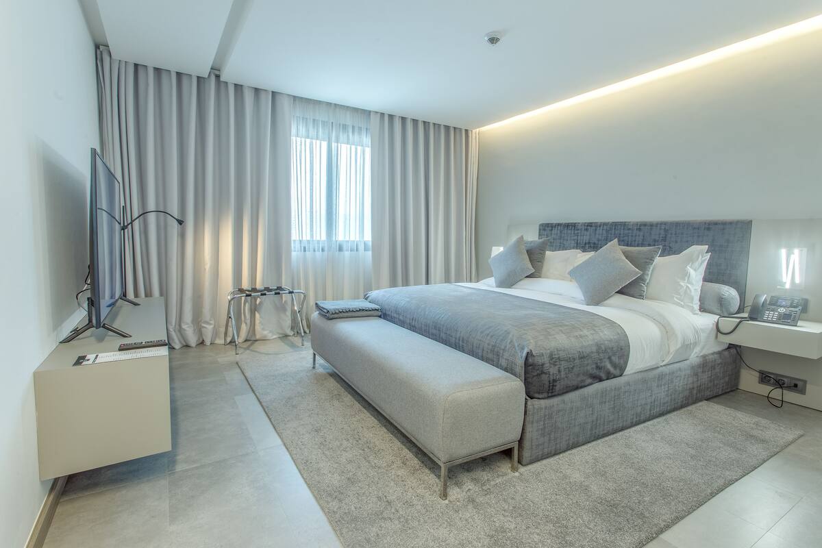 A modern bedroom with a large bed, bedside table, and a desk with a chair.