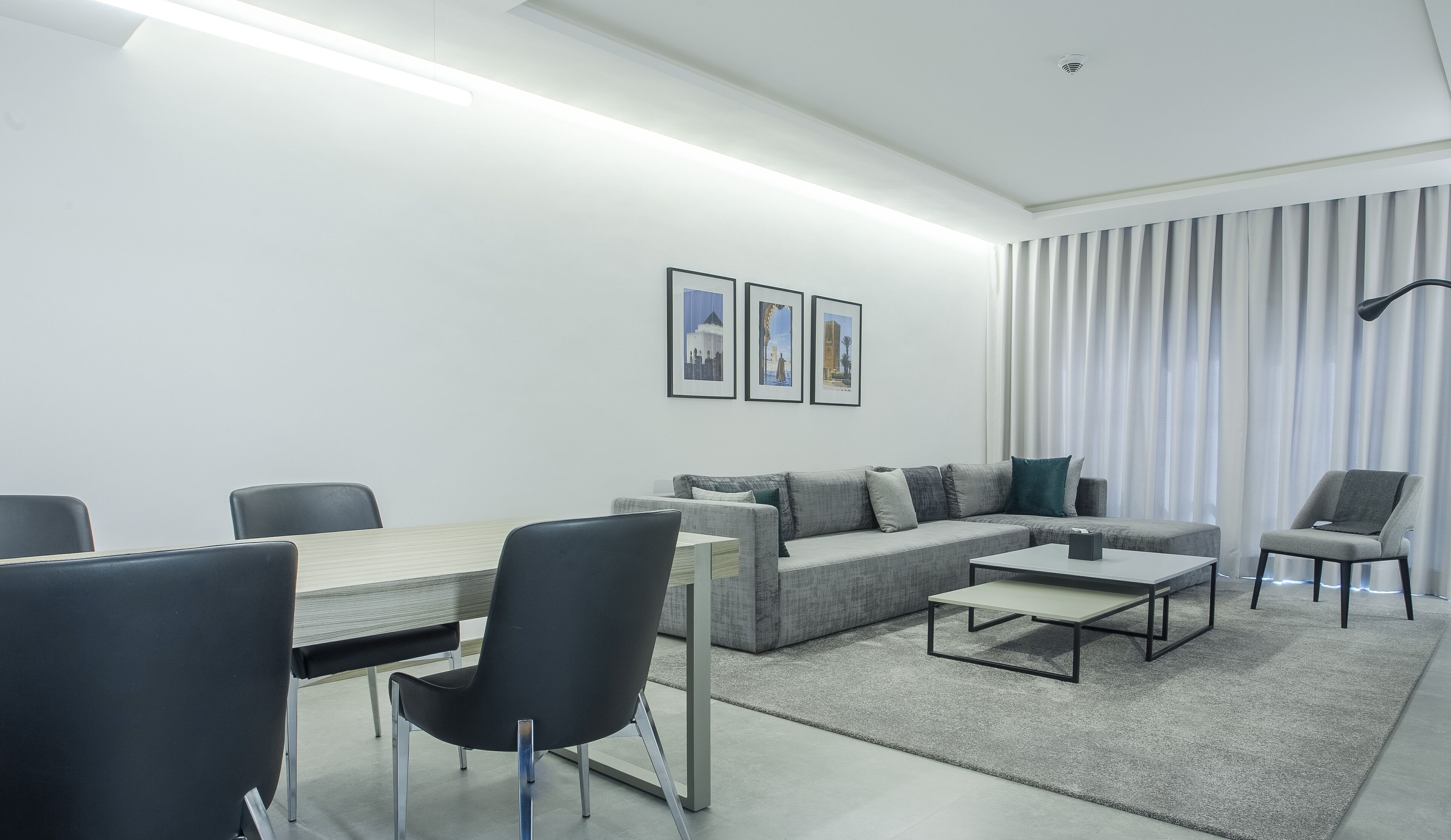 Una sala moderna con sofá, sillas, una mesa de centro y una mesa de comedor. Hay tres cuadros enmarcados en la pared.