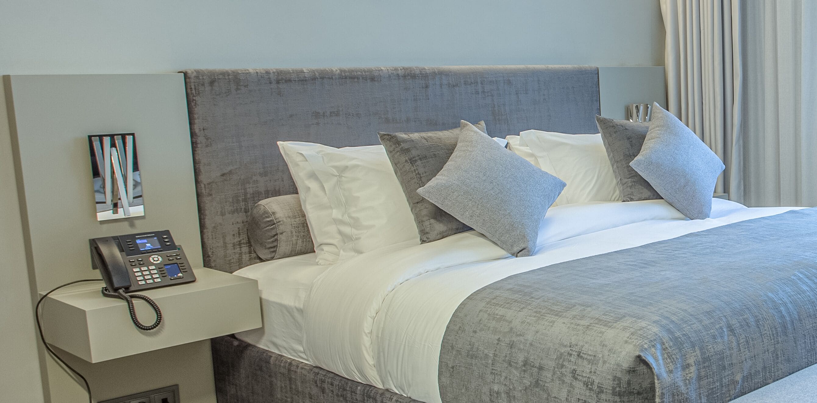 Habitación de hotel con cama, almohadas, mesita de noche con teléfono y una obra de arte en la pared.