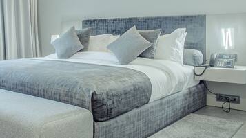 A modern bedroom with a large bed, grey bedding, and a bedside phone.