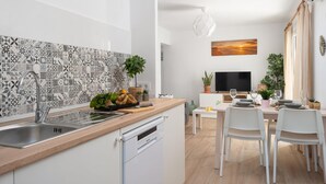 Una cocina moderna con salpicadero de azulejos, lavavajillas y comedor con sillas blancas y una mesa.