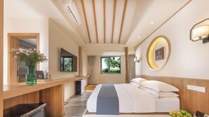 Habitación de hotel moderna con cama, escritorio, televisor y vista a zonas verdes.