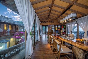 Un intérieur en bois avec un long couloir menant à un espace bar, de grandes fenêtres et une vue sur un bâtiment traditionnel à l’extérieur.