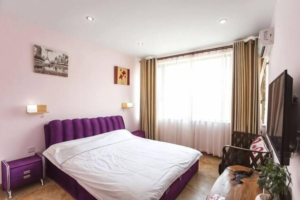 A hotel room with a bed, a nightstand, a chair, a television, and a window with curtains.