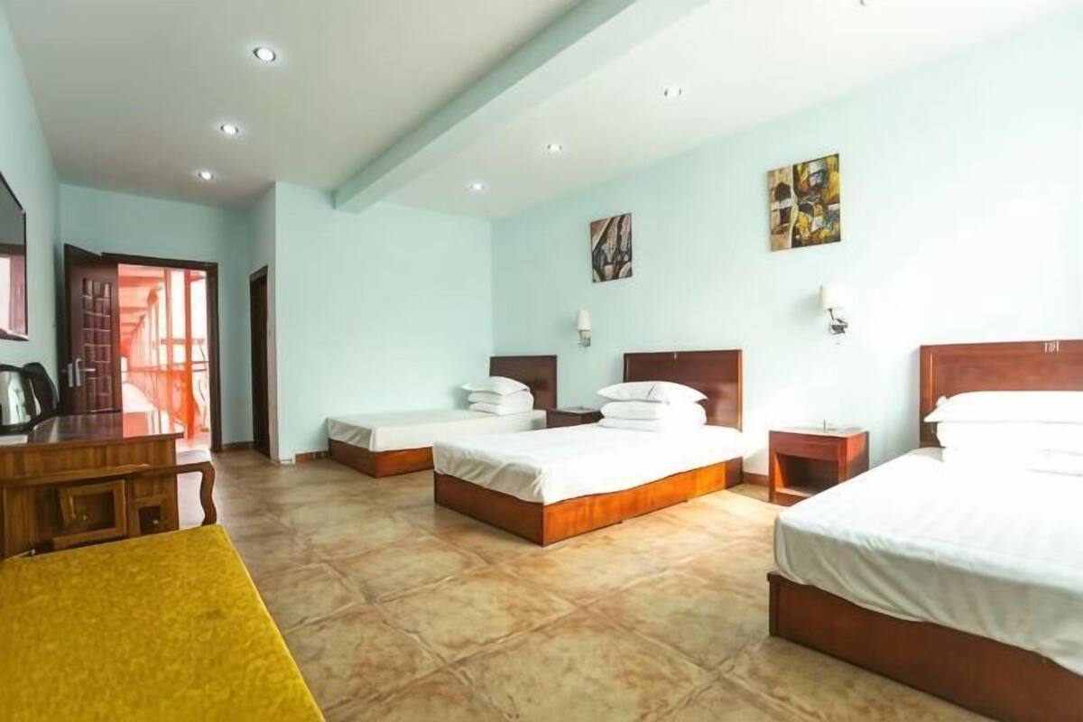 A hotel room with three beds, a wooden desk, and a yellow chair.