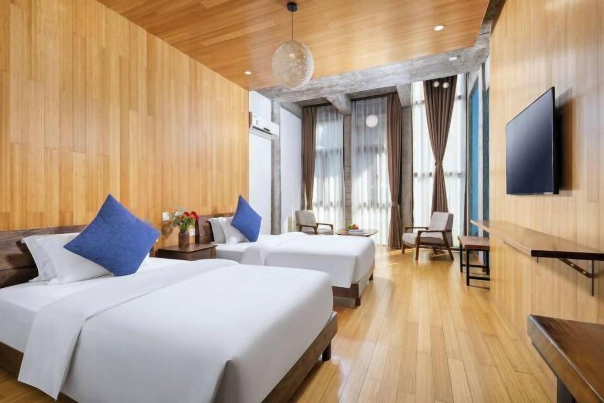 Habitación de hotel con dos camas, suelo de madera, televisión de pantalla plana y un ventanal con cortinas.