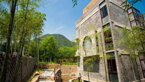 Um edifício tradicional com um caminho de pedra, bambus e montanhas ao fundo.