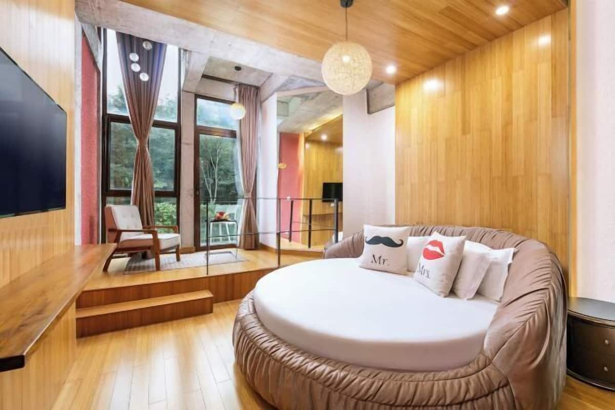 Un dormitorio con una cama grande, piso de madera, televisor y vistas al exterior.