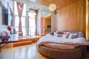 A modern bedroom with a circular bed, wooden flooring, and a view of a cityscape through large windows. - Zhujiuju Hostel (Deqing)