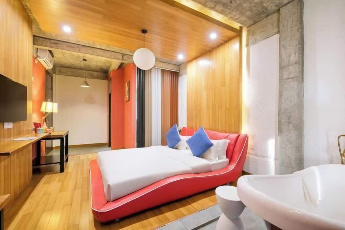 Una habitación de hotel moderna con una cama curvada, una zona de estar, un escritorio y una bañera grande.