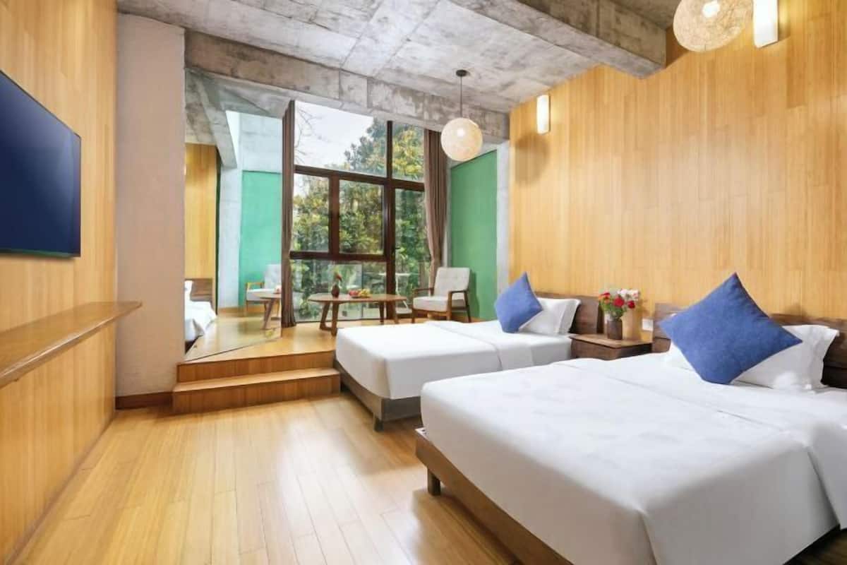Habitación de hotel con dos camas, piso de madera, un ventanal grande y un balcón con mobiliario exterior.